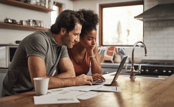 Par sitter vid köksbordet och planerar tillsammans framför en laptop