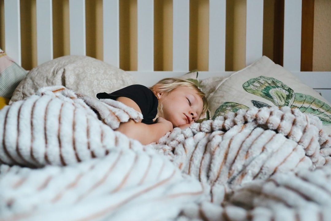 Litet barn sover i en säng under en mjuk, randig filt